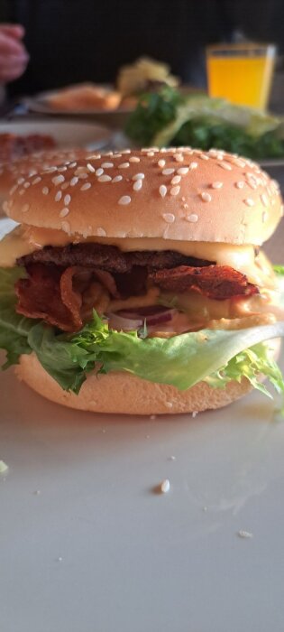 Hamburgare med sallad, ost och bacon på en tallrik, med suddig bakgrund av en annan måltid.