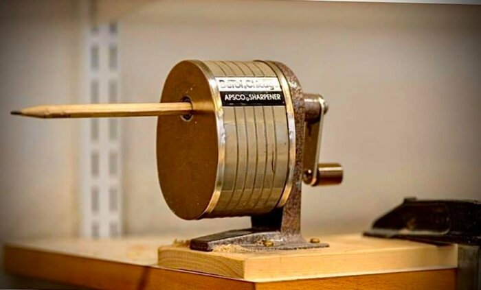 Vintage bordsmonterad pennvässare i metall med nysvarvad penna i cederträ.