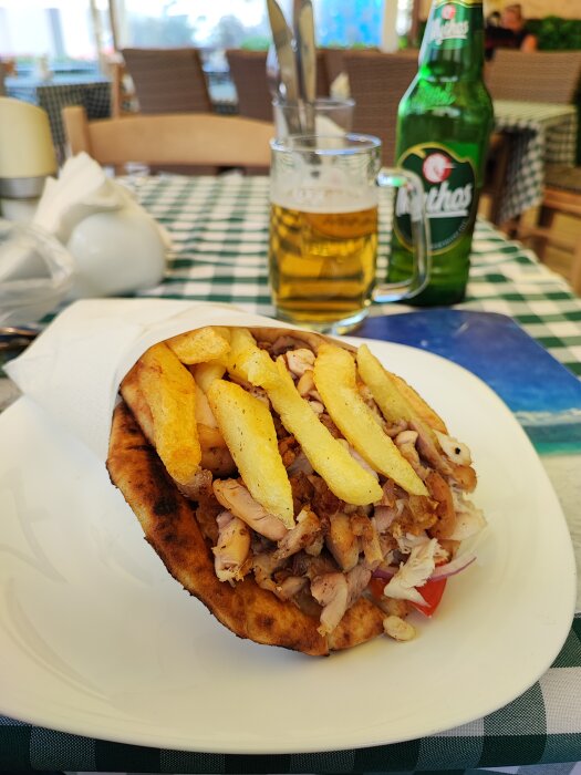 Gyros i pita med pommes frites och en flaska Mythos öl i bakgrunden på en vit tallrik.