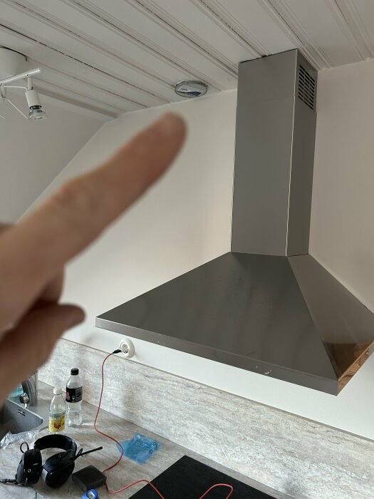 Köksrenovering med nyinstallerad köksfläkt, oisolerade kablar och person som pekar mot fläkten.