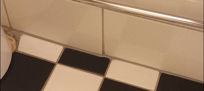 Nya silikonfogen i badrum, vita kakelväggar möter klinkergolv med en synlig ojämnhet i fogningen.