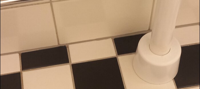 Närbild på ny silikonfog vid toalettens fot där svartvit klinker möter vit kakelvägg i ett badrum.