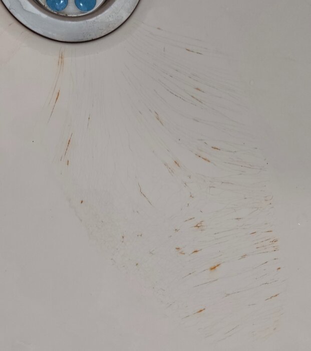 Närbild av badkarets avlopp med repor och rödaktiga fläckar efter rengöring för mögel.