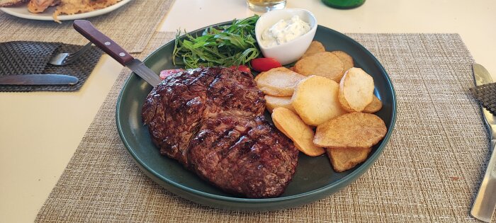 Grillad entrecote med pommes och sidosallad på en tallrik.