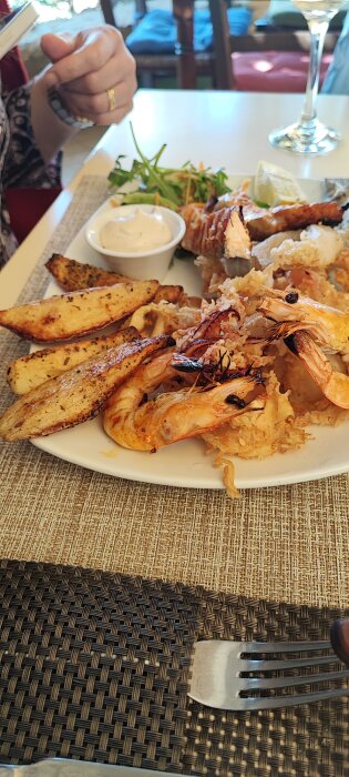 En tallrik med seafood platter, bestående av grillade räkor, calamari och dippsås, serveras på ett restaurangbord.