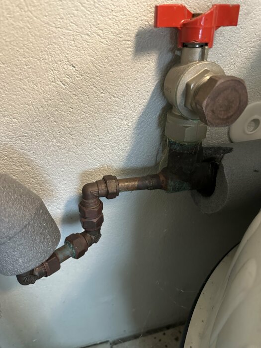 Vattenledning med rör av 28 mm diameter med röda och bruna ventiler och kopplingar mot en grå vägg.