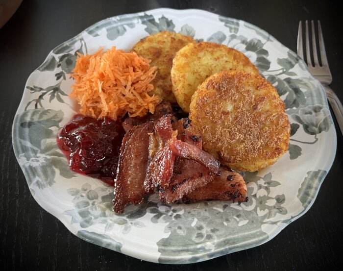 Tallrik med stekt fläsk, två potatisbullar, riven morot och en klick lingonsylt.