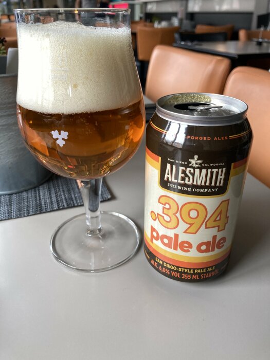 Alesmith 394 pale ale-öl i glas med skumkrona bredvid tom burk på bord.