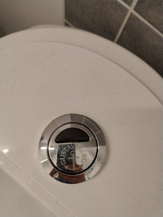 Närkontakt av toalettstolens spolknapp med Gustavsberg-logotyp, indikerar potentiell läckagekälla och svagt vattenflöde.