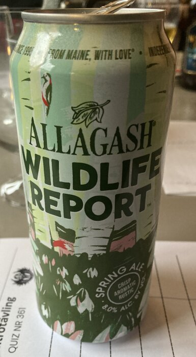 Allagash Wildlife Report Spring Ale ölburk med blommönster och text, på ett bord.