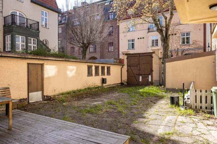 Innergård till byggnad med odlingsyta och träterrass, omringad av historiska byggnader i Östermalm, Stockholm.