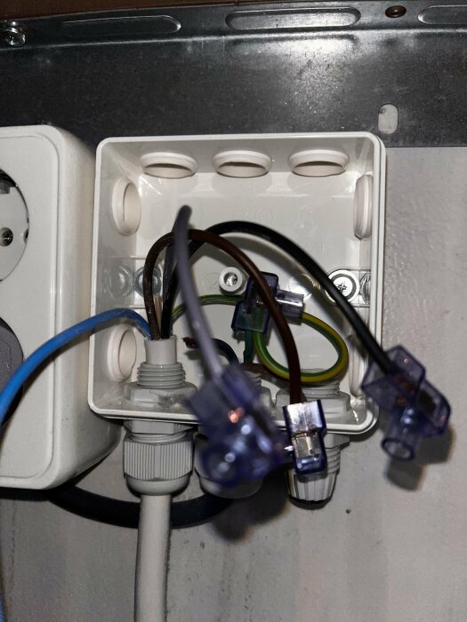 Öppen kopplingsdosa med kabelgenomföring och flera elektriska kablar och ändhylsor i olika färger.