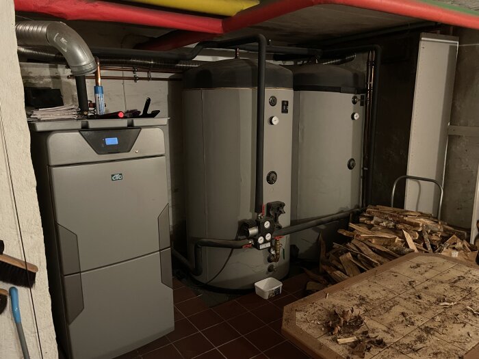 Värmesystem i källare med värmepump, ackumulatortankar, ved och kopplingar.
