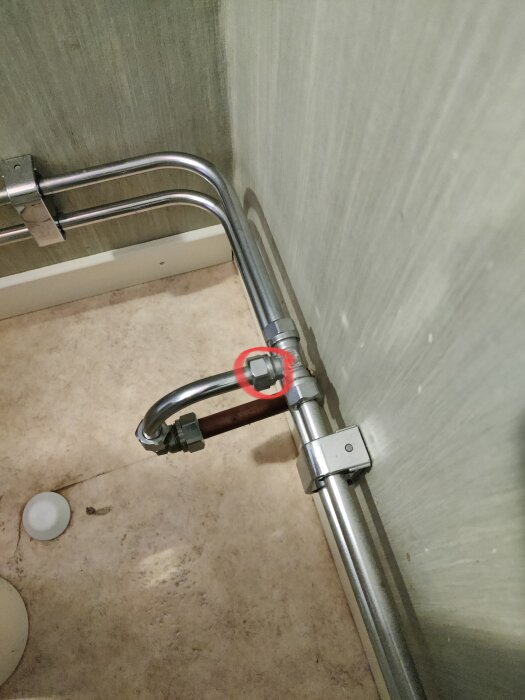 Vattenrör med T-koppling och röd ballofix installerad vid vägg och golv i en byggnad.