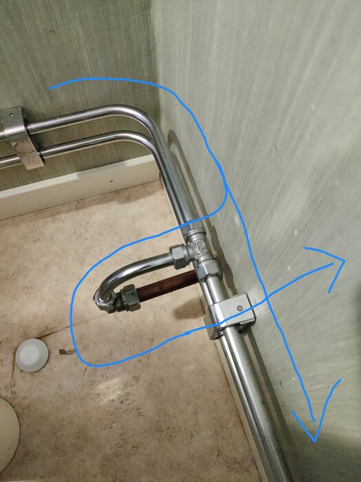 Vattenrör med T-koppling i badrum markerad med blå pilar som visar riktningen till garage.