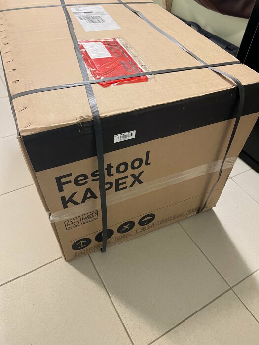 Oöppnad låda märkt "Festool KAPEX" bunden med svart rem, levererad och redo för unboxing.