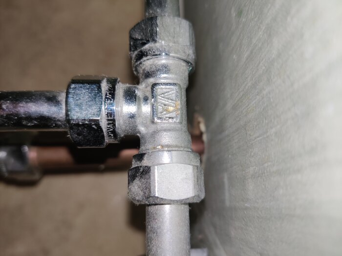 Vatette-märkt rörkoppling i rostfritt stål, med en närbild av rör och koppling mot en betongvägg.