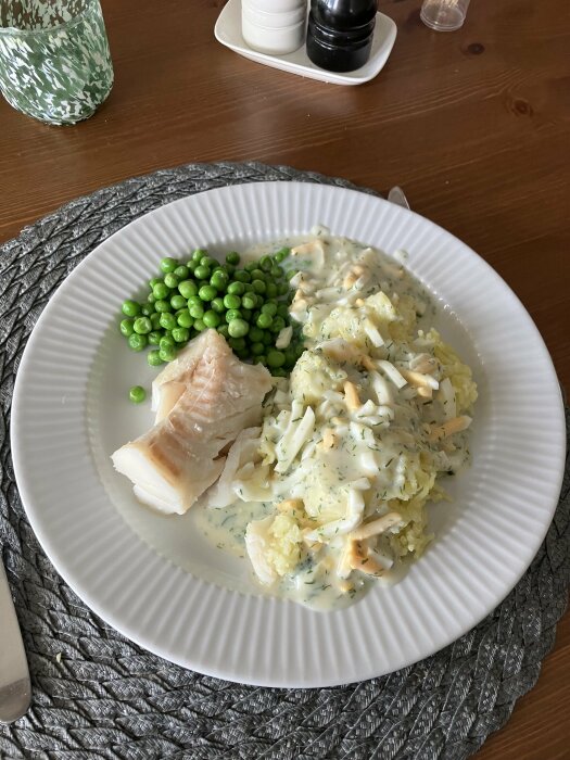 Tallrik med torskrygg, äggsås och gröna ärtor på ett matbord.