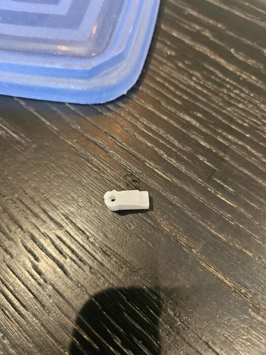 Enspröjsclips av vit plast på ett mörkt träbord, vid sidan av en blå plastbehållare.