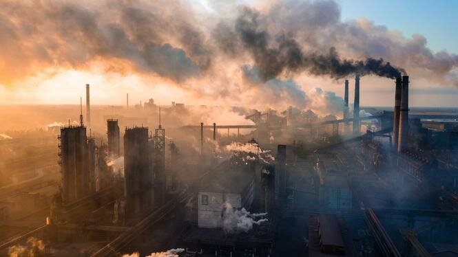 Industriområde med skorstenar som släpper ut rök mot en solnedgång.