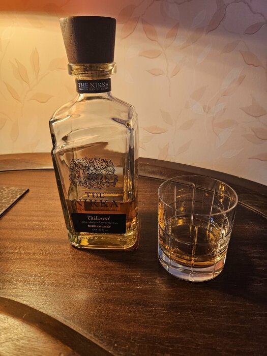Flaska av The Nikka Premium Blended Whisky bredvid ett whiskyglas på ett träbord.