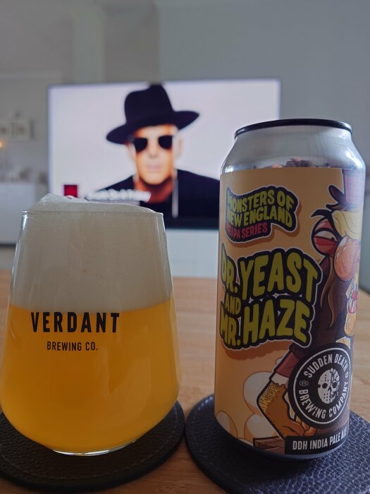 Ölglas med öl från Verdant Brewing Co. och burk från Sudden Death Brewing med texten "Dr. Yeast and Mr. Haze" framför TV-skärm.