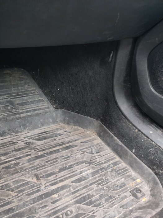 Bilens golv med inbyggda öglor för bilstol synliga nära bilens säte och en smutsig golvmatta.