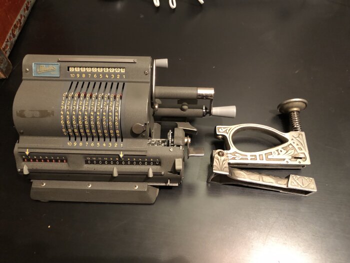 Gammal mekanisk räknemaskin och en häftpistol på ett bord.