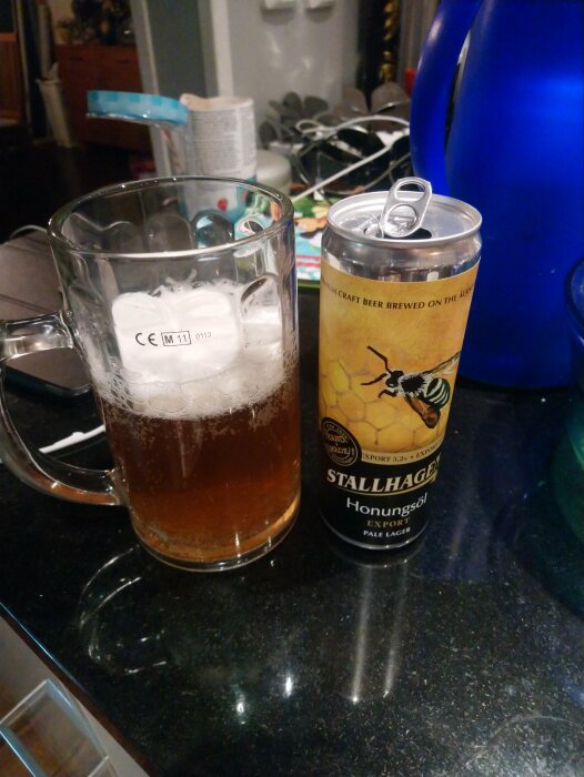 Ölglas fyllt med Stallhagen honungsöl och en burk av samma öl på en köksbänk.