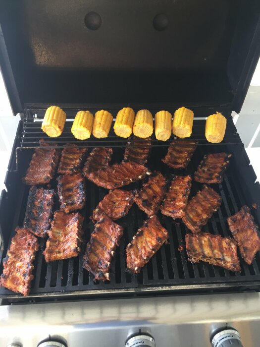 Grillade baby back ribs och majskolvar på en grill, marinade glänser på köttrik yta.