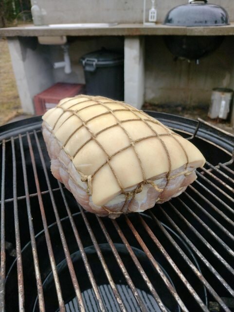 Bindad skinka redo för rökning på grillgaller med webergrill i bakgrunden.