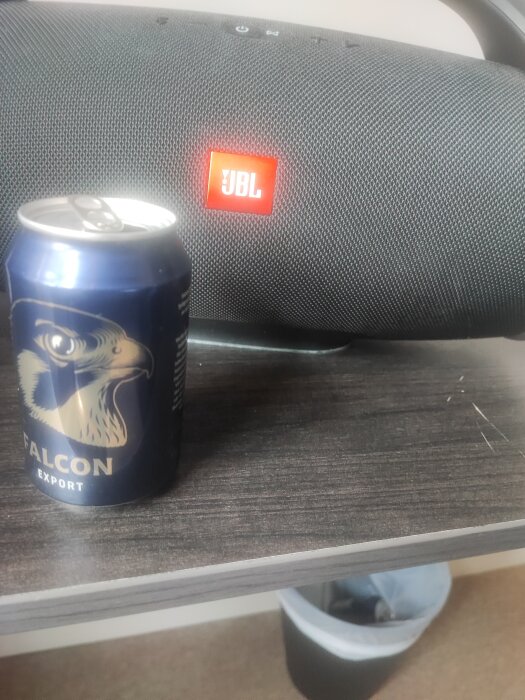 En burk Falcon Export öl framför en JBL-högtalare på ett brunmönstrat bord.