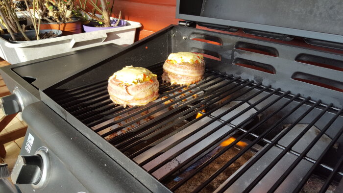 Burgare av nötfärs fyllda med grönsaker, omgivna av bacon och toppade med ost på en grill.