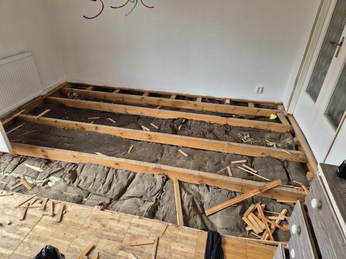 Upprivet golv i ett enplanshus visar träreglar och befintlig isolering mot betongplatta.