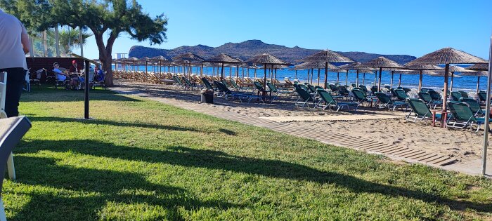 Solstolar och parasoller på en sandstrand med berg i bakgrunden på en solig dag.