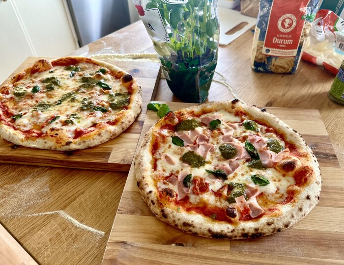 Två hemgjorda pizzor på skärbrädor, en med mozzarella och basilika, en med skinka och pesto.