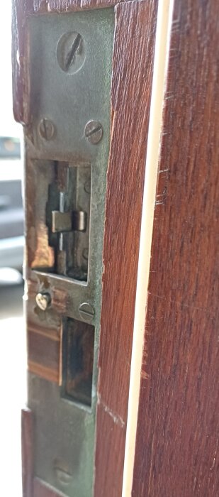 Närbild av en dörrkarm med en skruv som sticker ut från dörrlåsets inbyggda mekanism.