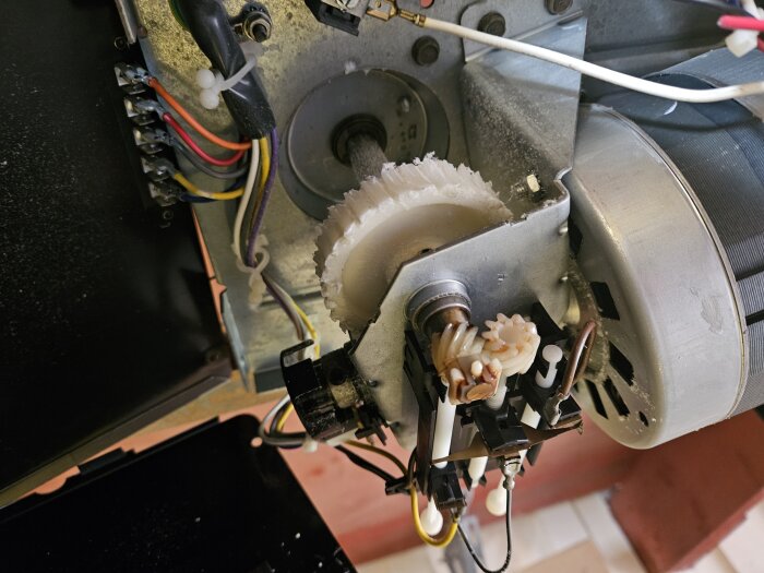 Söndermald plastkugghjul inne i en garageöppnare med synliga elektriska komponenter och kablar.