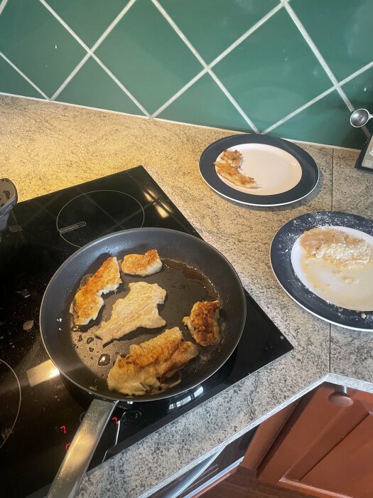 Stekpanna med kycklingfilébitar på spishäll, två tallrikar med matrester vid sidan.