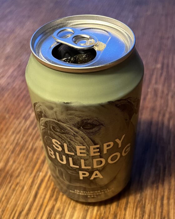 Öppnad ölburk av märket Sleepy Bulldog Pale Ale på ett träbord, med fokus på burkens öppning.