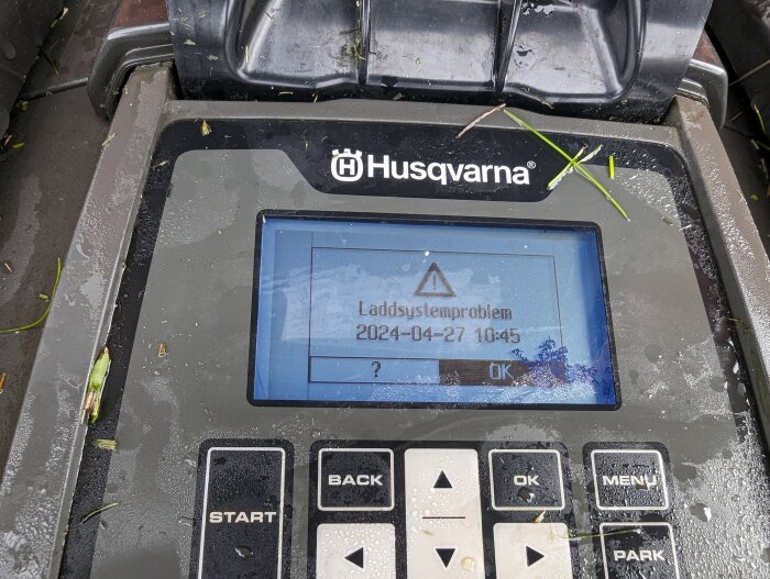 Husqvarna robotgräsklippares display med felmeddelandet "Laddsystemproblem" och datumstämpel.