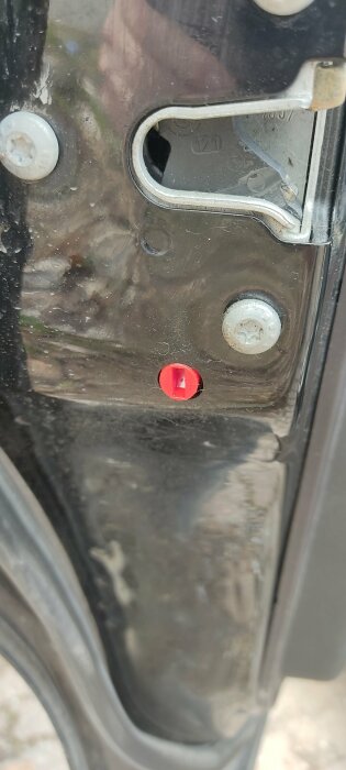 Röd barnspärrknapp i kanten av en öppen bildörr, vilken man vrider för att aktivera barnlåset.