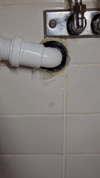 Avloppsrör som är olämpligt installerat och läcker vid anslutningen till väggen i ett badrum.