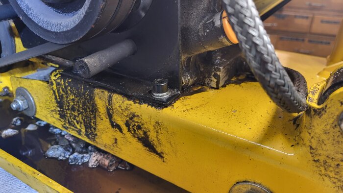 Närbild på en gul markvibrator som läcker olja, med synliga oljefläckar och stenar.