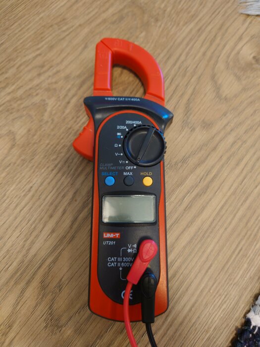 Digital multimeter med röd mätprob ansluten på träunderlag.