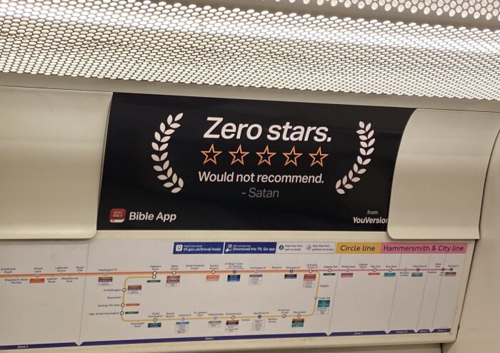 Reklamskylt för Bible App med recension "Zero stars. Would not recommend. -Satan", ovanför en tunnelbanekarta.