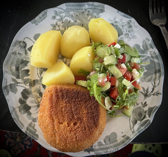 Panerad kalkon med ostfyllning, kokt potatis och fräsch sallad på ett mönstrat fat.