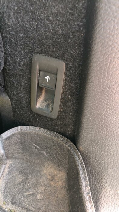 Elektrisk knapp för nedfällning av dragkrok i bil, smutsig och använt utseende.