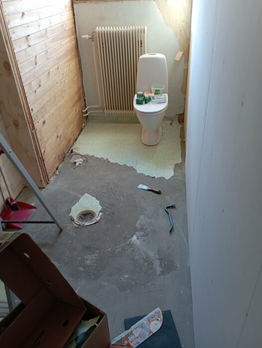 Renoveringsarbete i badrum med osatt klinkergolv, vit toalett och radiator under fönster.
