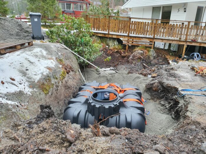 Installation av BDT-tank och septitank i utgrävd grop bredvid berg och hus med trädäck.